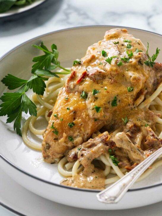 A plate with chicken and sundried tomato sauce on a bed of pasta.