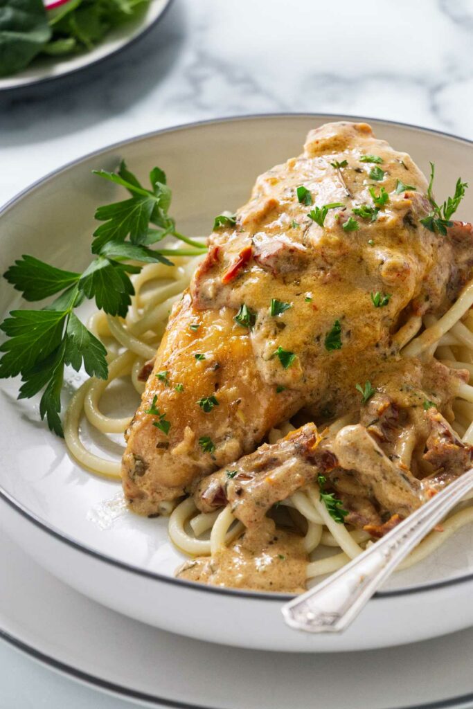 A plate with chicken and sundried tomato sauce on a bed of pasta.