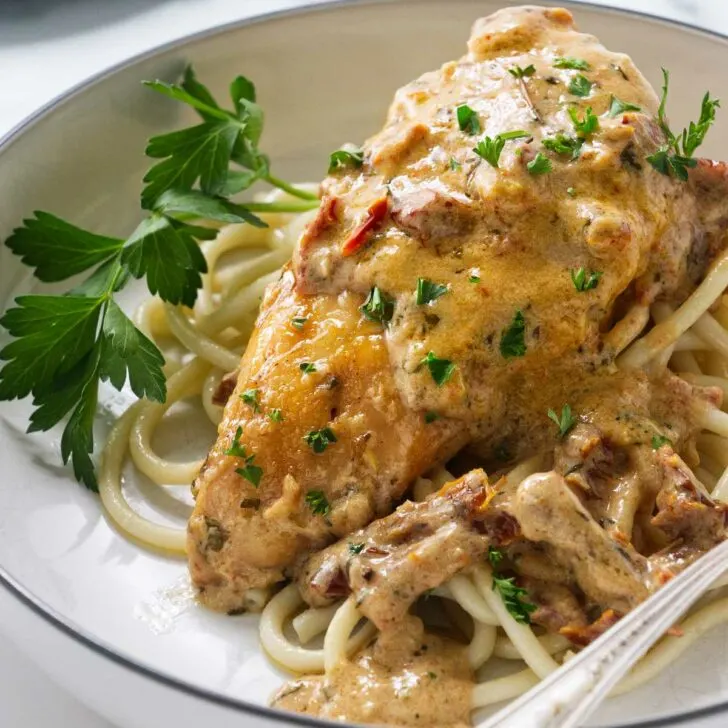 A plate with chicken and sundried tomato sauce on a bed of pasta.