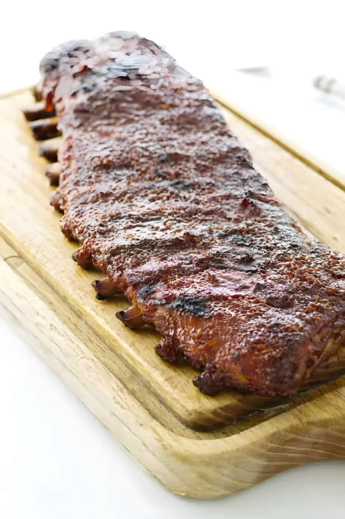 A slab of baby back ribs on a cutting board.