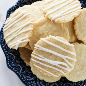 A pile of crisp lemon cookies with a drizzle of icing on the top of each cookie.