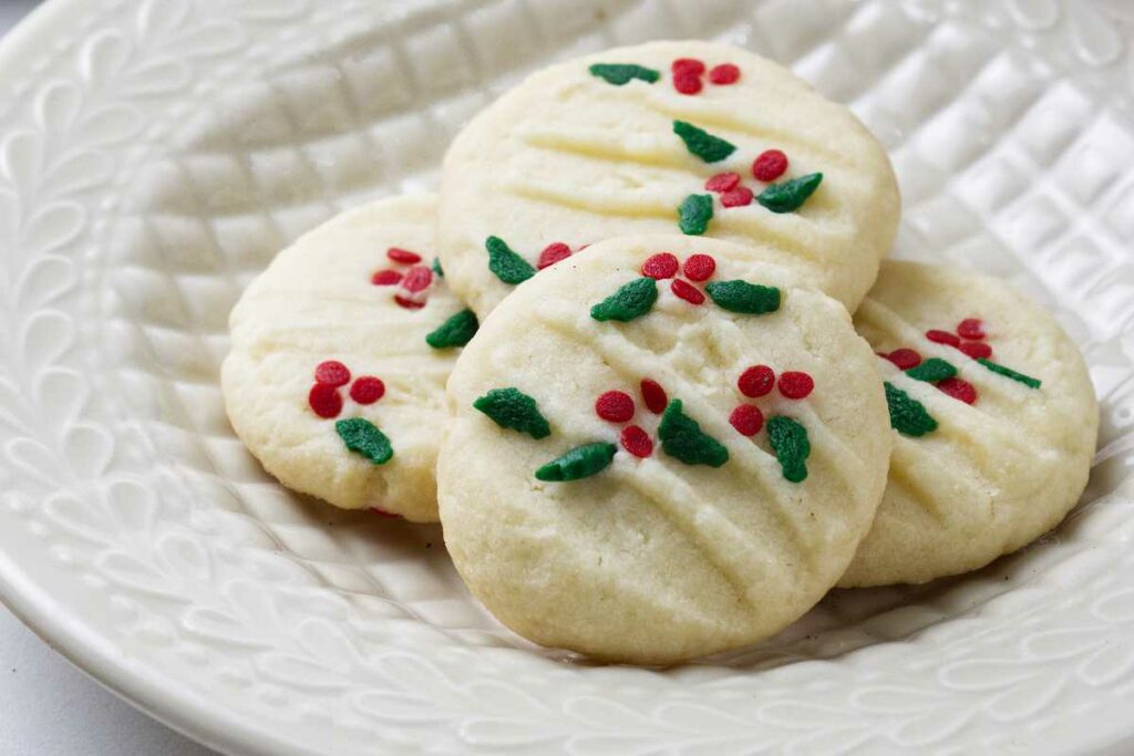 Four shortbread Christmas cookies with sprinkles on top.