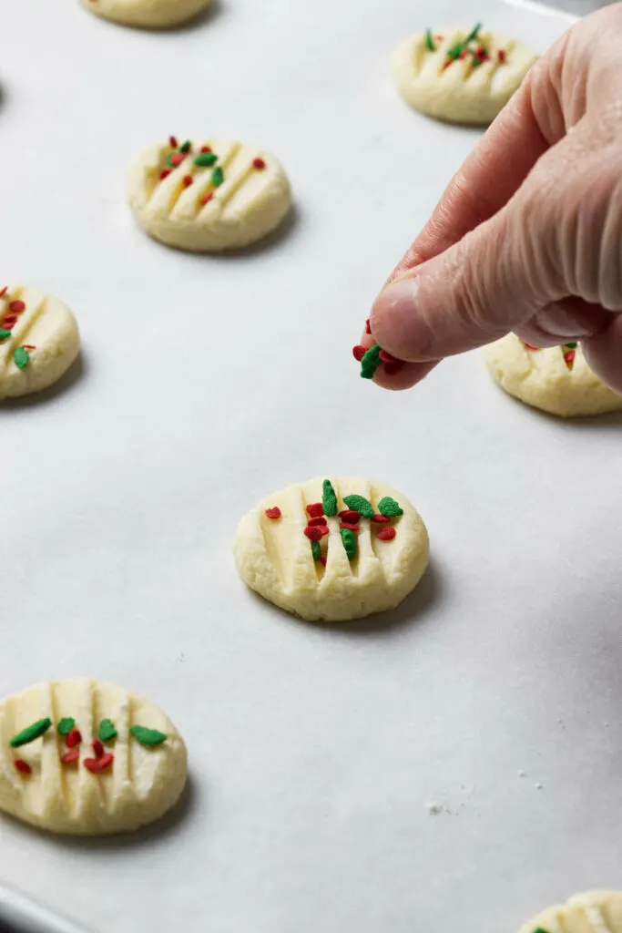 Adding sprinkles to drop shortbread cookies on a baking sheet.