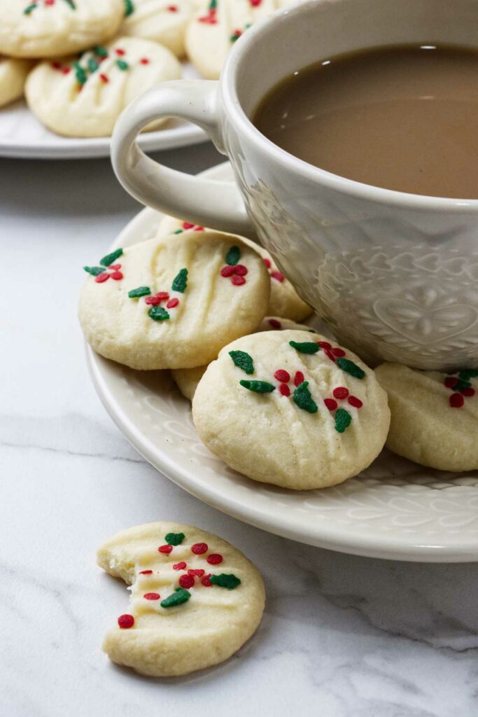 Whipped shortbread cookies on a plate with a cup of coffee.