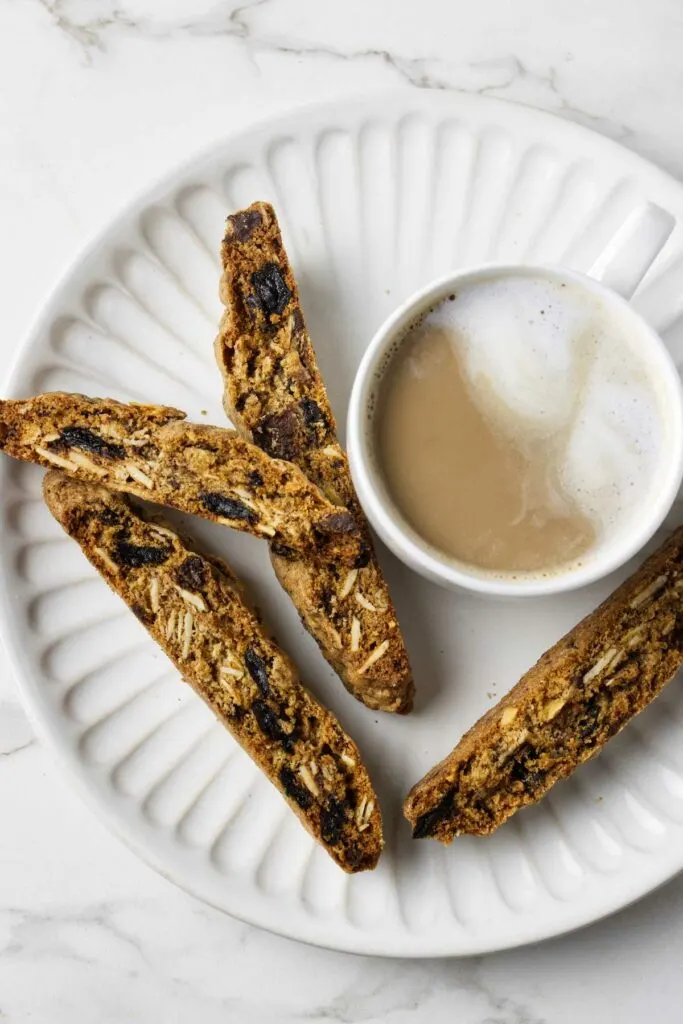 Four whole wheat biscotti cookies on a plate with a cup of coffee.