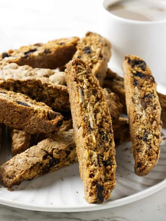 Several whole grain biscotti cookies on a plate with a cup of coffee in the background.