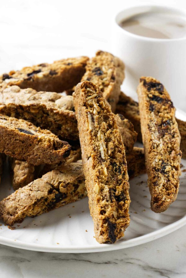 Several whole grain biscotti cookies on a plate with a cup of coffee in the background.