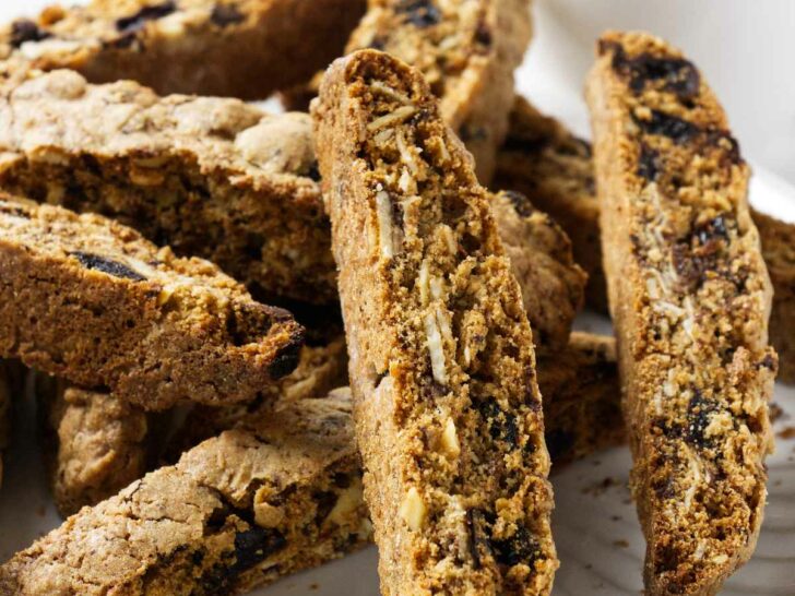 Several whole grain biscotti cookies on a plate with a cup of coffee in the background.