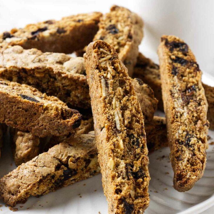 Several whole grain biscotti cookies on a plate with a cup of coffee in the background.