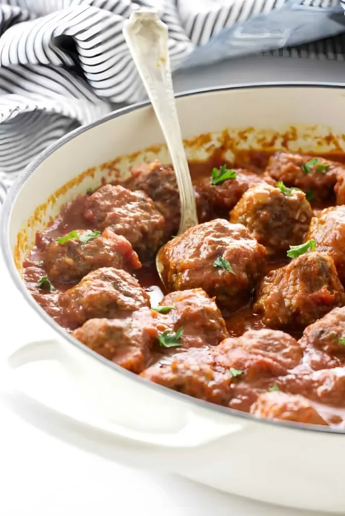 Meatballs and marinara sauce in a skillet with a spoon.