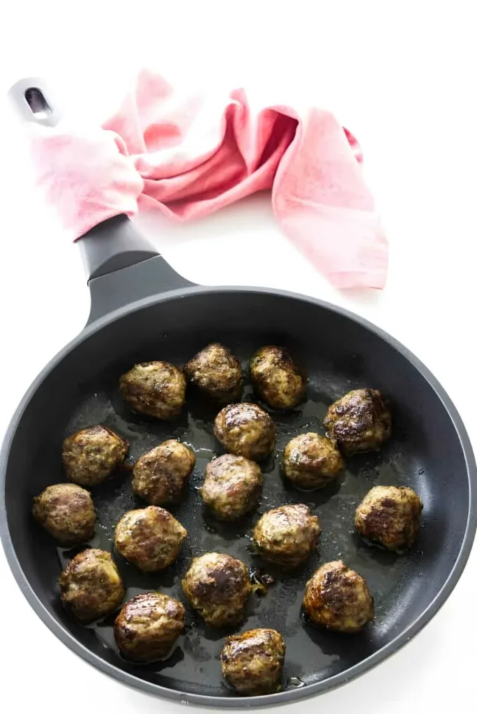 Several meatballs browning in the skillet.