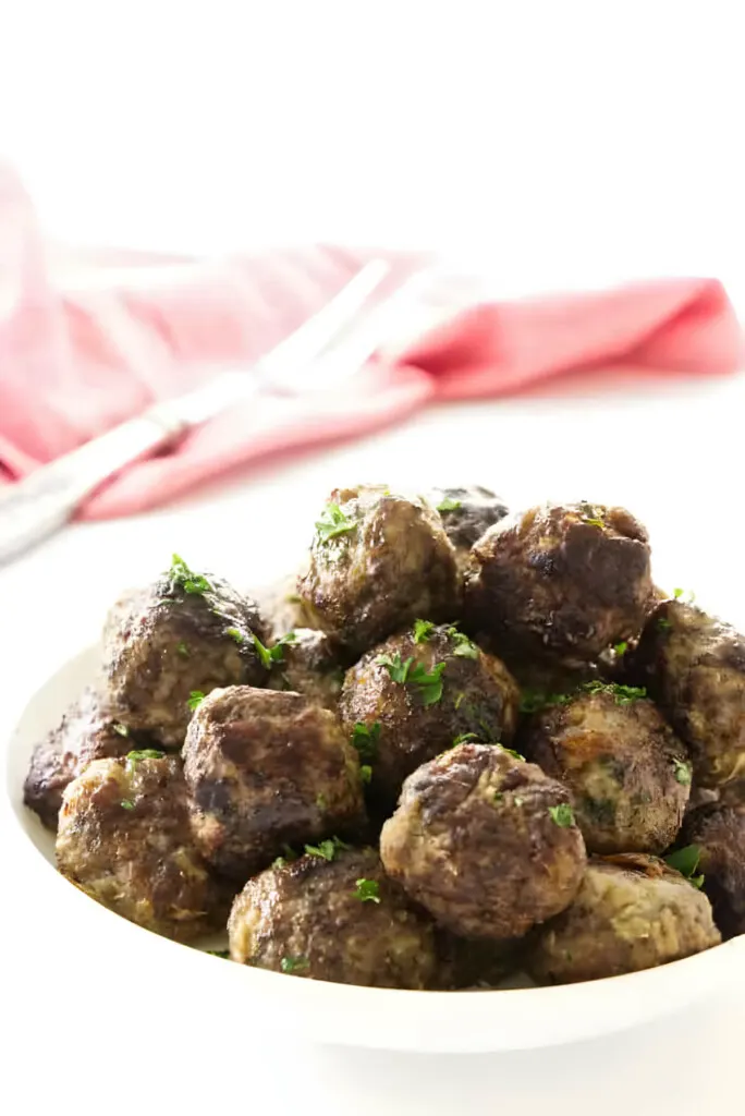 A dish filled with several meatballs with a fork in the background.