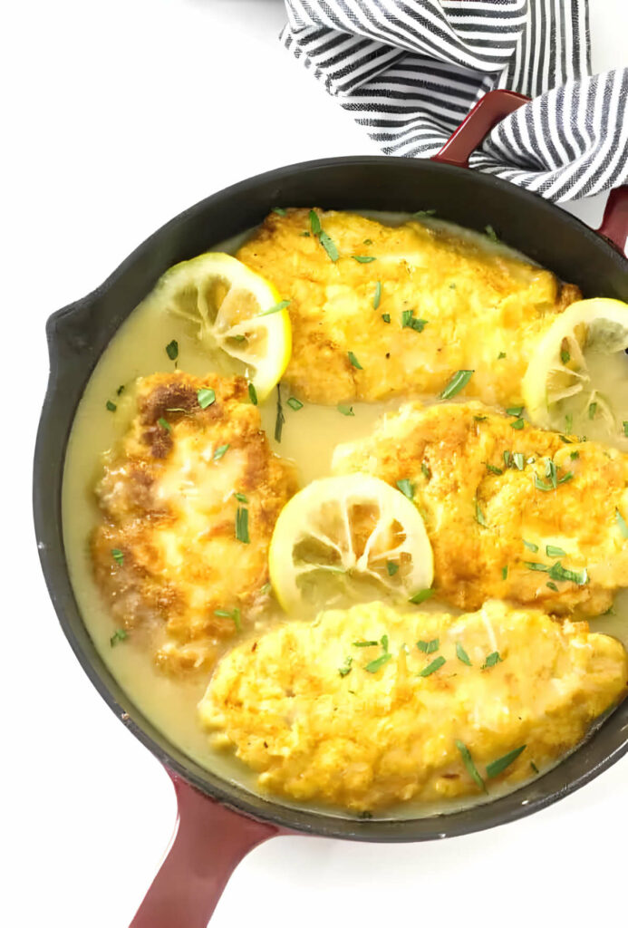 A skillet with chicken cutlets in a lemony sauce.