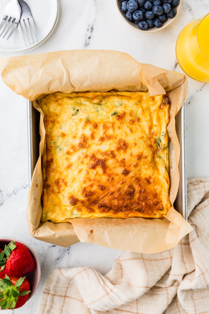 A cottage cheese and eggs casserole in a baking pan next to berries.