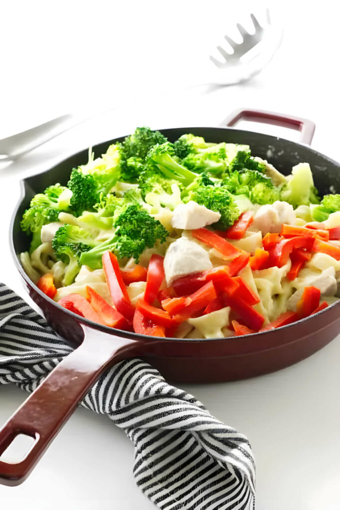 Tossing broccoli and chicken in a skillet with pasta and creamy alfredo sauce.