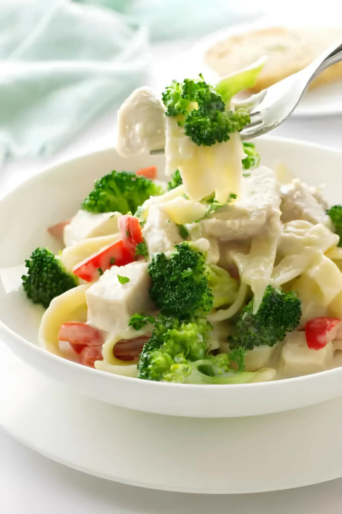 A fork with a bite of broccoli chicken pasta.