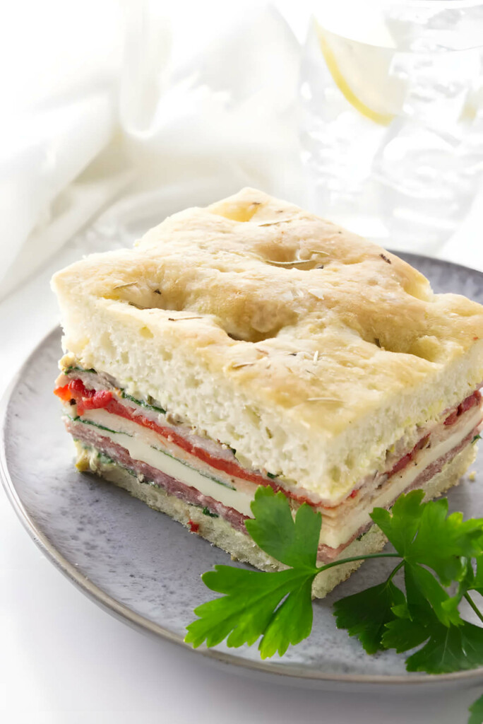 A slice of a sandwich made with focaccia bread, meats, and cheese.