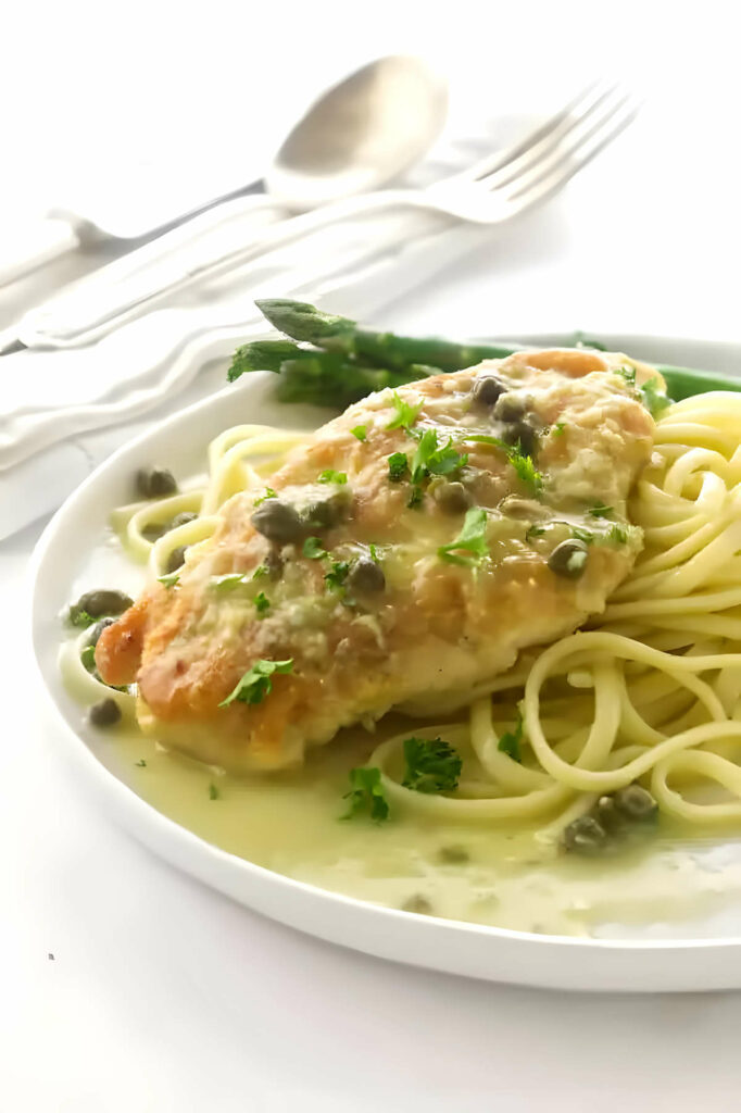 Pan fried lemon chicken on some pasta covered in sauce and capers.