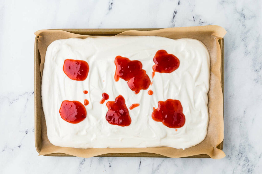 Dropping dollops of strawberry jam on top of the yogurt.