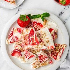 A plate with filled with thin wedges of frozen yogurt bark next to some fresh strawberries.