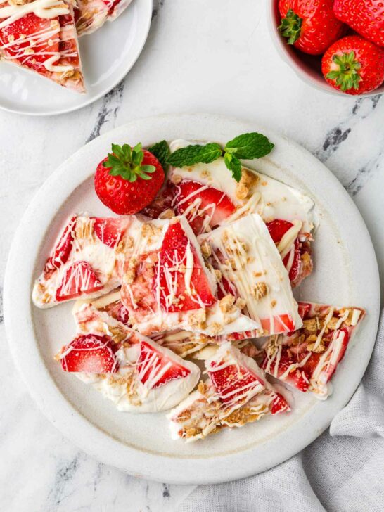 A plate with filled with thin wedges of frozen yogurt bark next to some fresh strawberries.