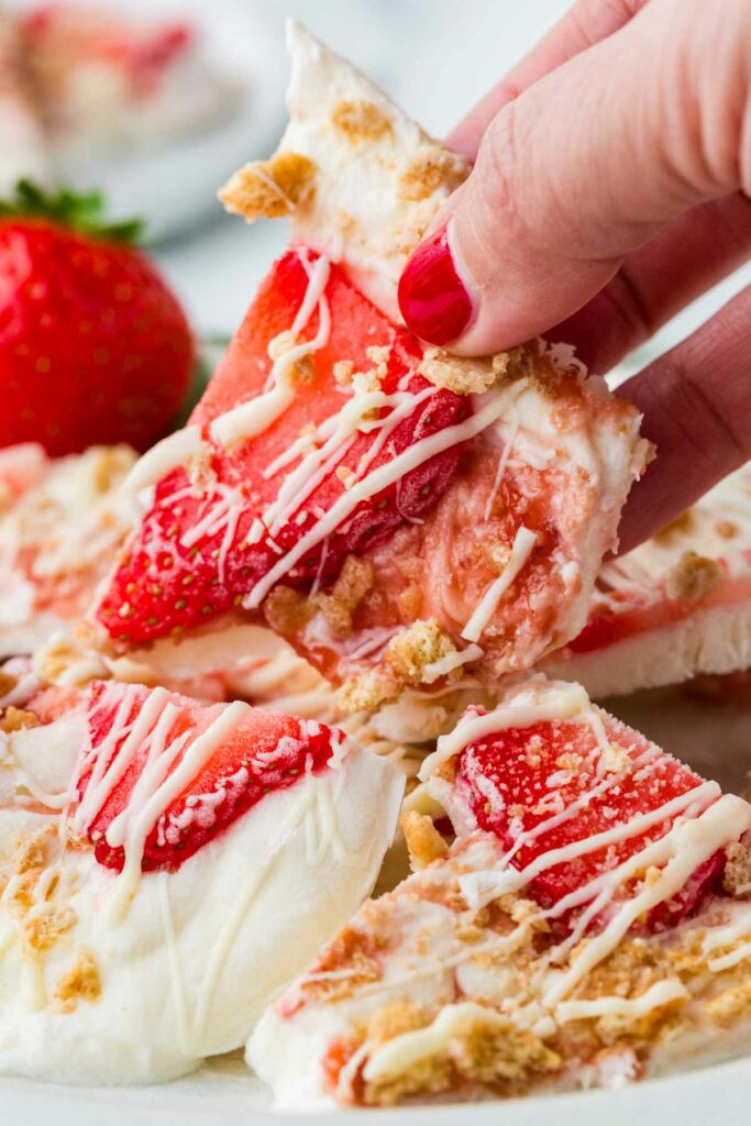 A hand grabbing a wedge of frozen Greek yogurt bark with strawberries and cookie crumbles on top.