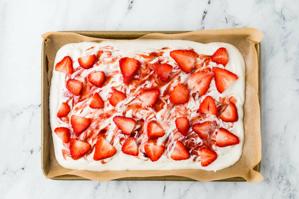 Adding slices of strawberries to the yogurt bark.