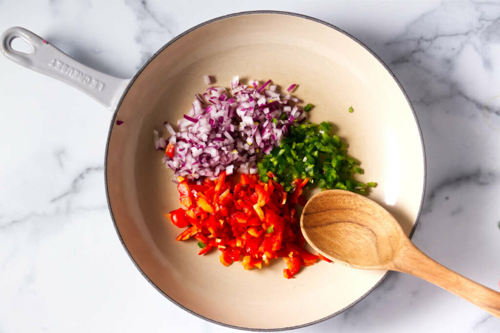 Adding onions red bell peppers and green bell peppers to a skillet.