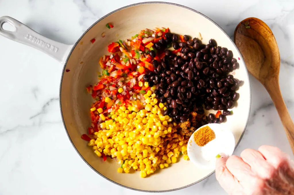 Placing corn, black beans and spices in the skillet with the sauteed veggies.