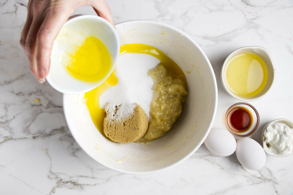 Adding butter, sugar, eggs and sour cream into the mixing bowl with mashed bananas.