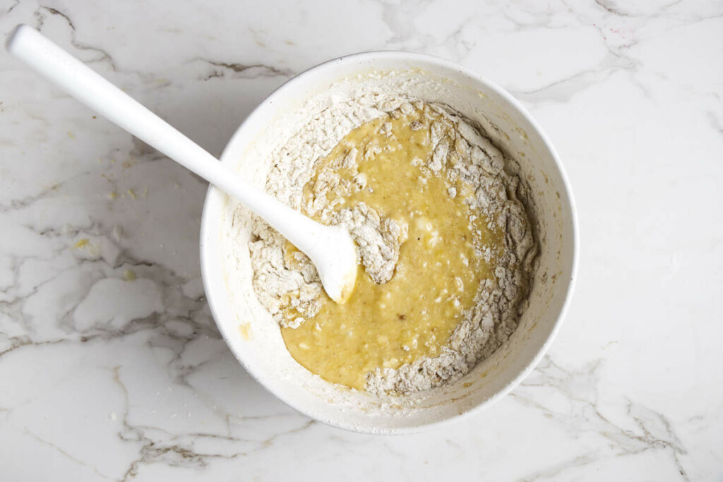 Using a spatula to fold the flour mixture into the banana bread batter.