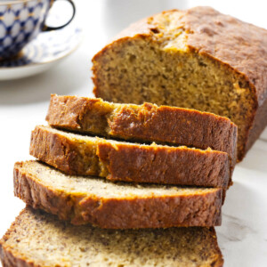 A loaf of sour cream banana bread next to a cup of coffee.