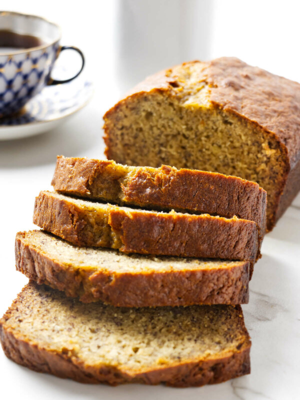 A loaf of sour cream banana bread next to a cup of coffee.