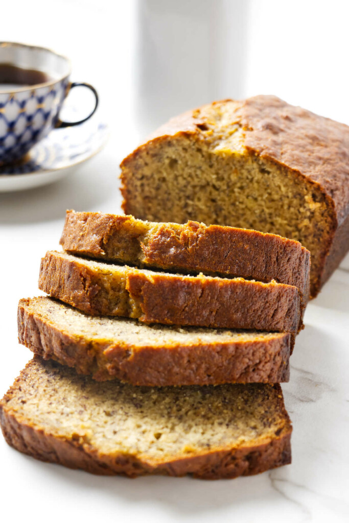 A loaf of sour cream banana bread next to a cup of coffee.