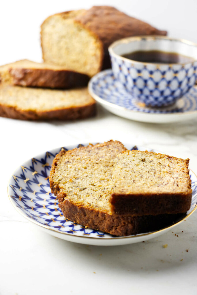 Two slices of banana bread on a plate in front of a cup of coffee.