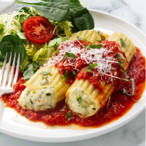 A dinner plate with cheese manicotti and a green salad.