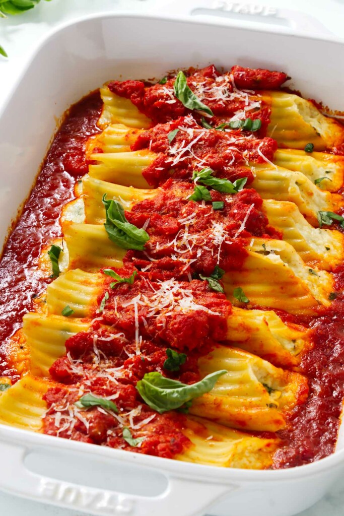 A baking dish with hot ricotta manicotti and marinara sauce.