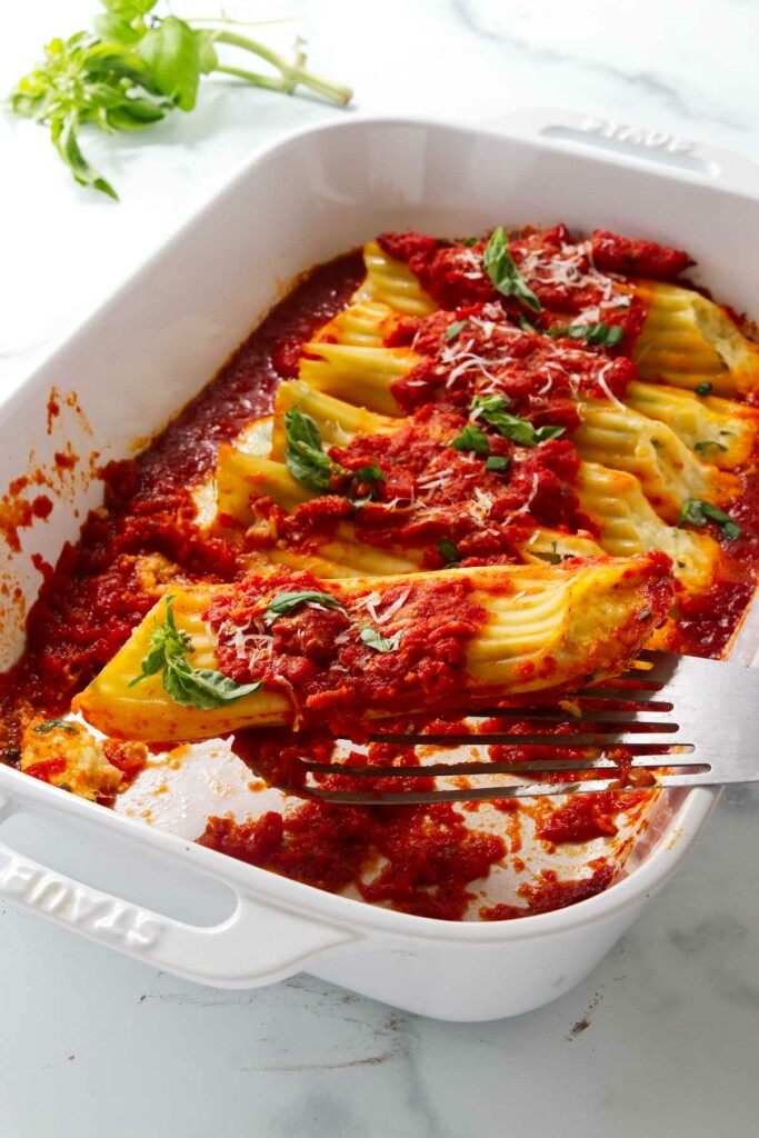 A spatula lifting a manicotti pasta from a baking dish.