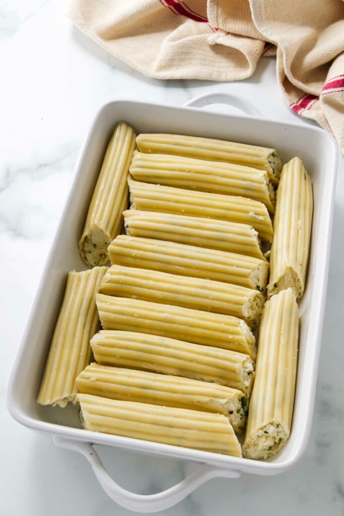 Placing fourteen cheese filled manicotti in a baking dish.