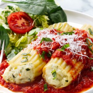 Two cheese manicotti on a dinner plate next to a green salad.