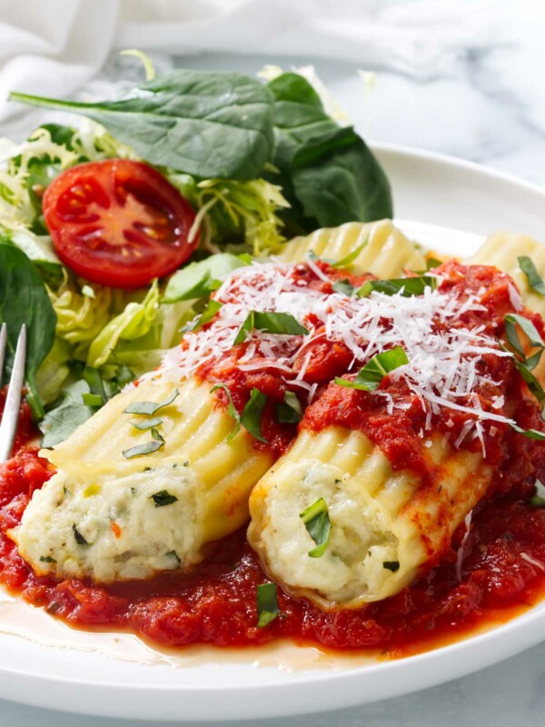 Two cheese manicotti on a dinner plate next to a green salad.