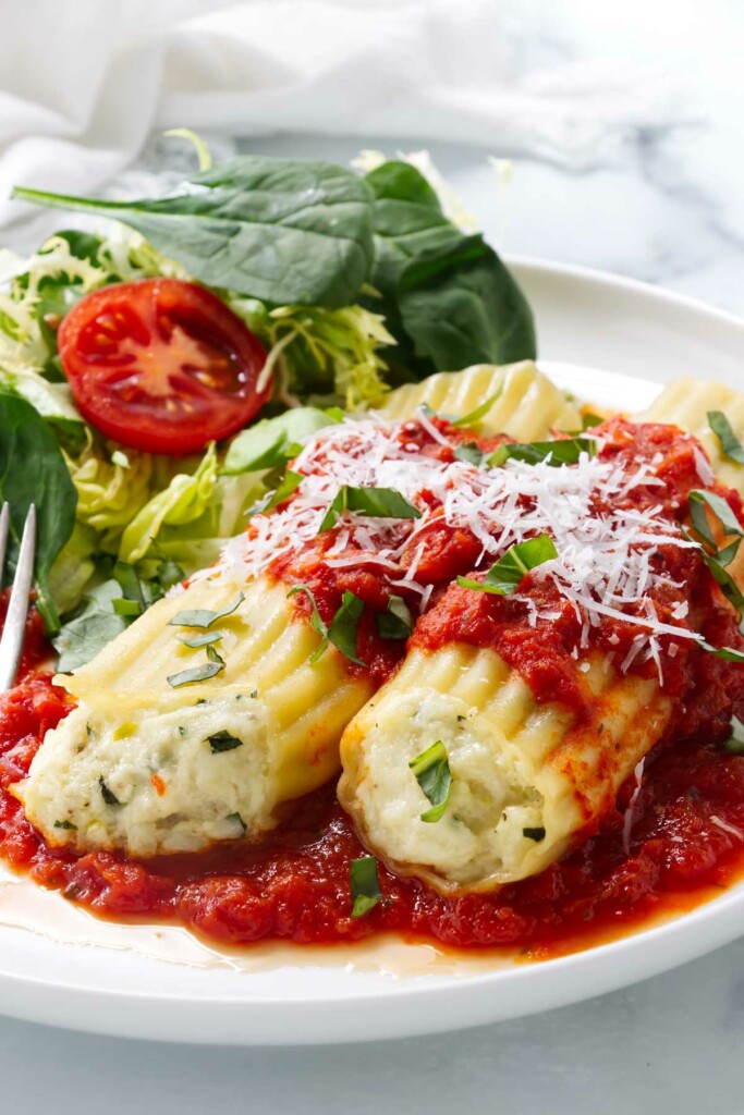 Two cheese manicotti on a dinner plate next to a green salad.