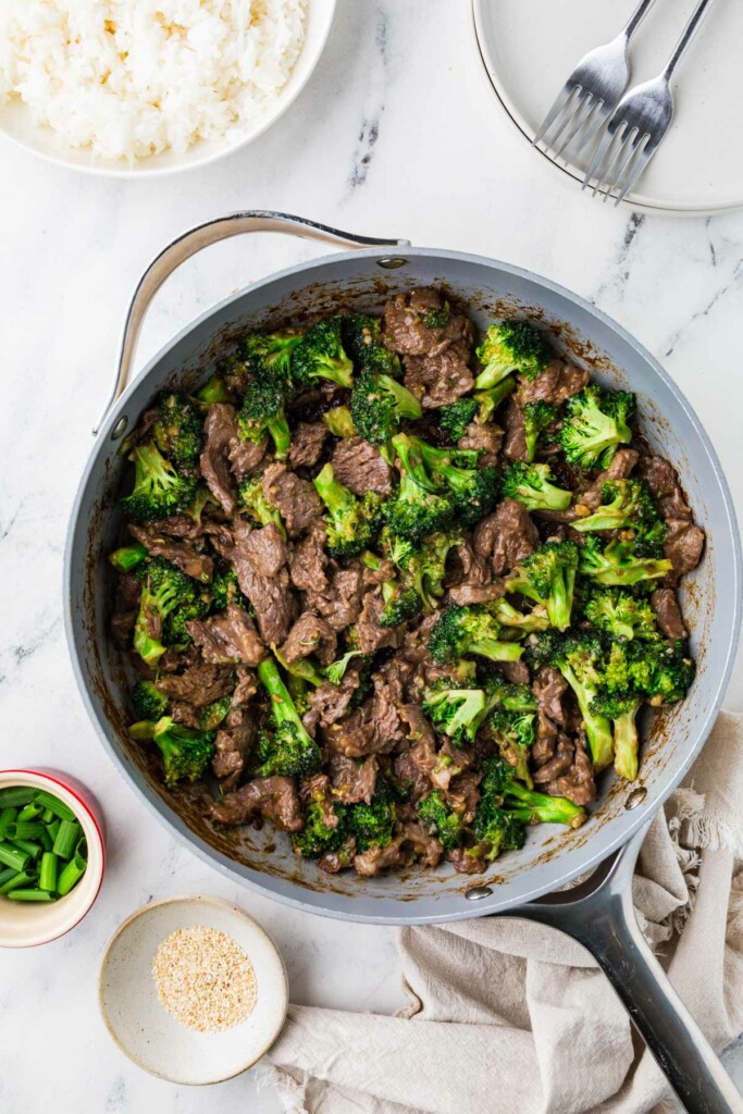 A skillet filled with broccoli and beef next to a bowl of rice.