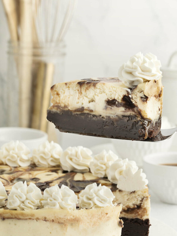 A spatula lifting a slice of a cheesecake with a brownie crust.