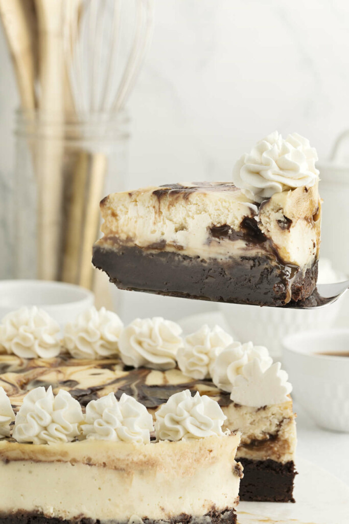 A spatula lifting a slice of a cheesecake with a brownie crust.