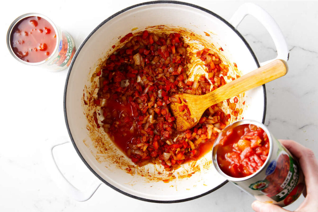 Adding tomatoes to the soup base with the onions and red bell peppers.