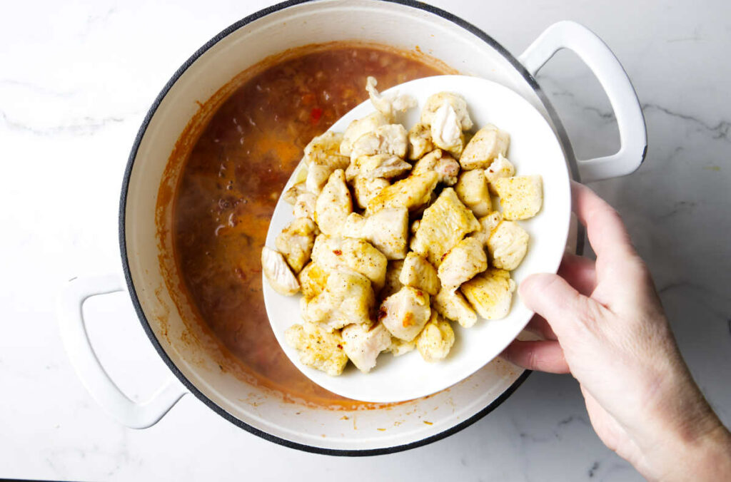 Adding the browned chicken back to the soup pot.