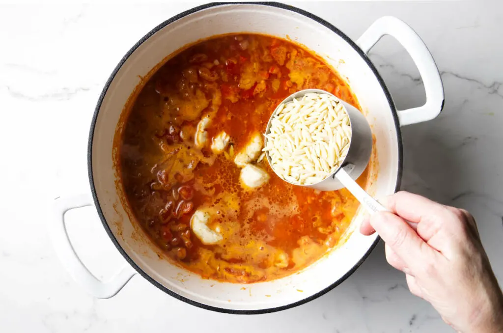 Stirring the orzo pasta into the soup broth.