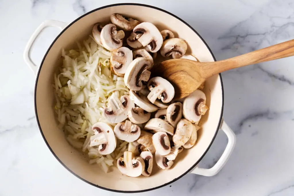 Adding onions and mushrooms to the skillet.