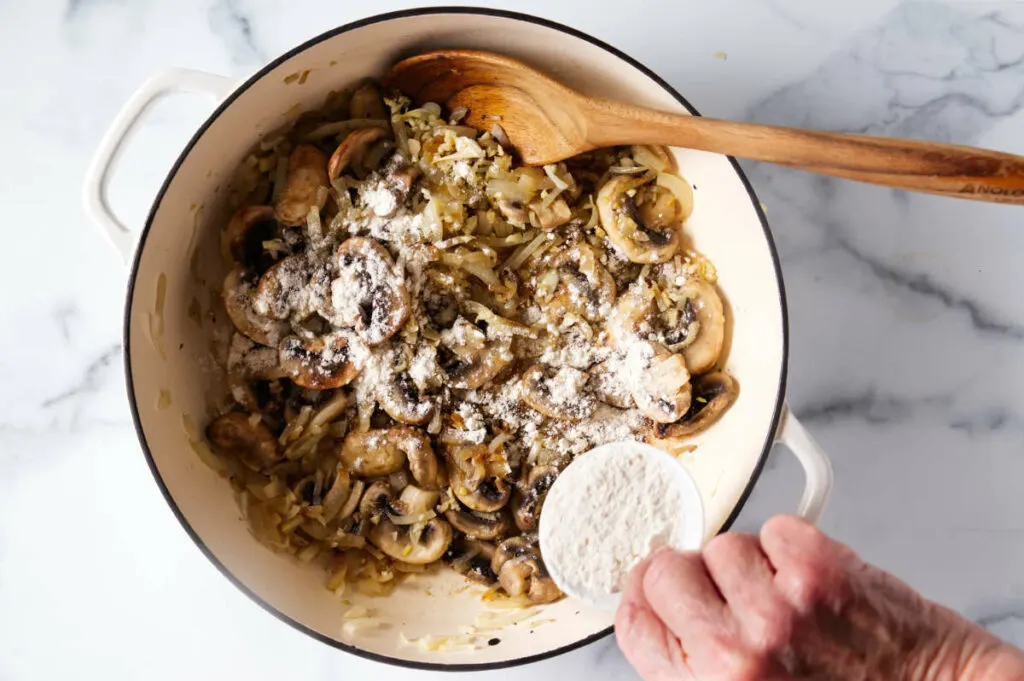 Adding flour to the sauteed mushrooms.